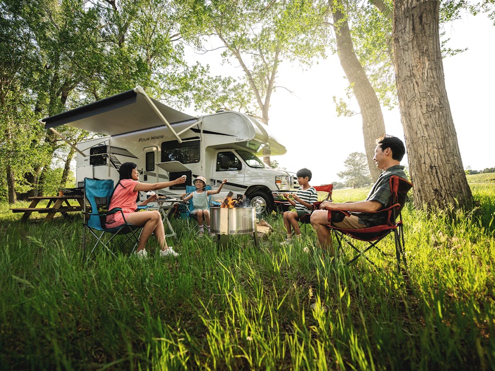 Family resting outside of Class C RV on sunny day